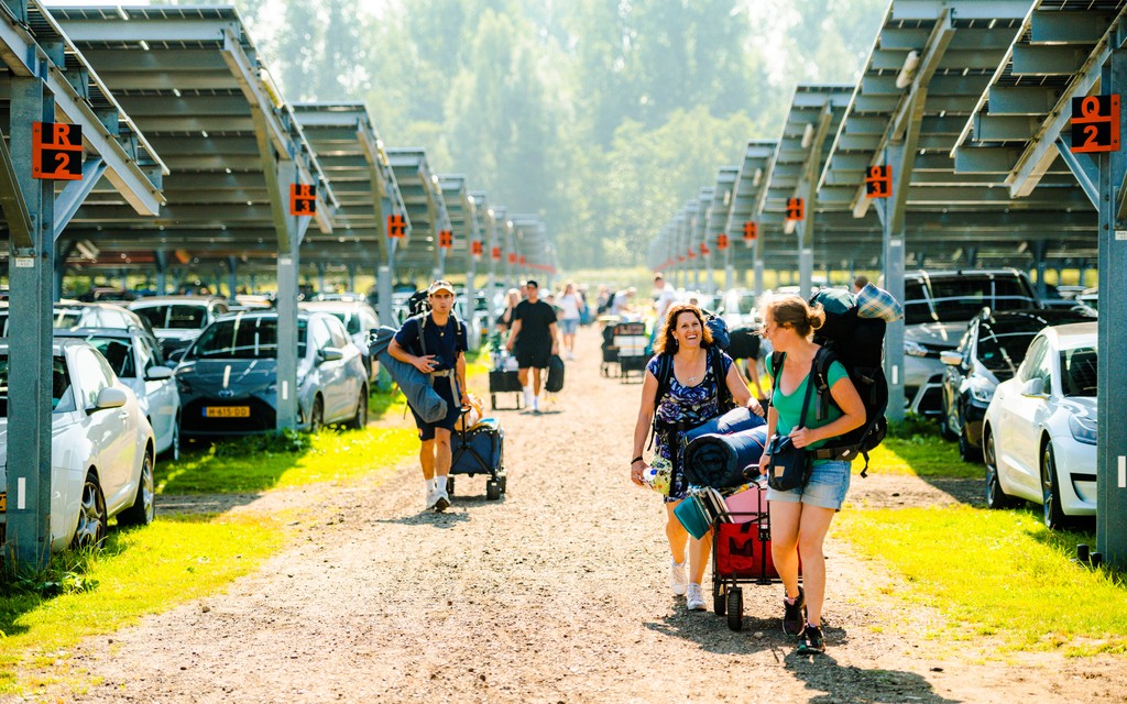Bezoekers lopen met bolderkar over parkeerterrein Bezoekers lopen met bolderkar over parkeerterrein